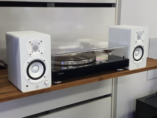 Turntable with white speakers on a wooden shelf against a white wall.