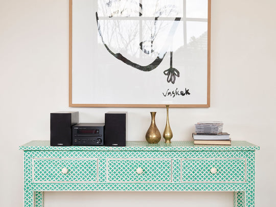 The Yamaha MCRB270D Micro HIFI in silver sitting on a teal blue wooden cradenza next to artfully arranged vases and a stack of cd's